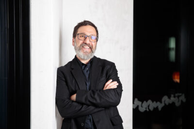 an author photo of Dr Tim Sharp, who is standing against a wall with his arms crossed, smiling at the camera