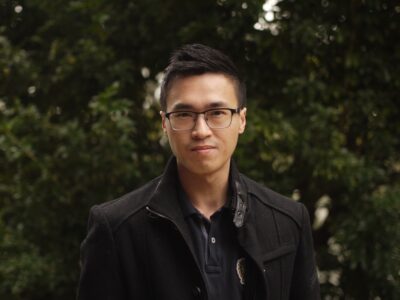 An author photograph of Siang Lu, who is looking directly at the camera, while standing in front of some trees.