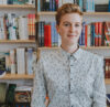 A photograph of Tace Kelly standing in front of a bookshelf.